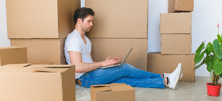 a man surrounded by boxes searching for movers Ocoee FL has to offer on his laptop