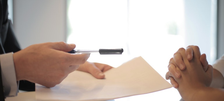 A cropped image of a man giving a pen and a paper to a woman;