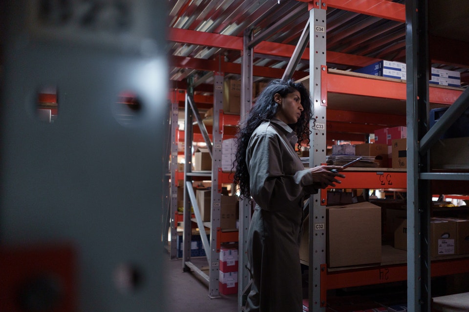 A woman wearing a gray uniform in a storage unit;