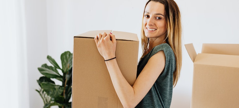 A smiling woman carrying a moving box