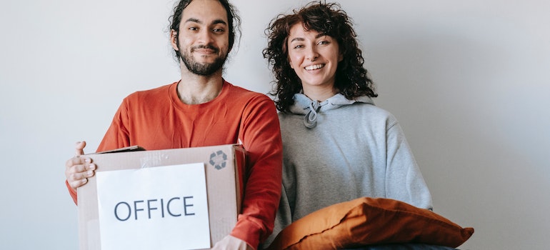 A man and a woman holding a box labeled as office;
