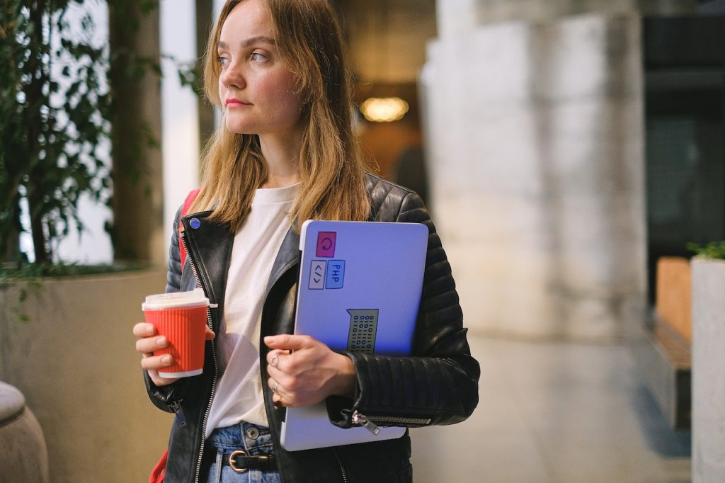 A young student holding her laptop and a cup of coffee.