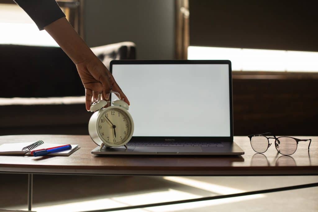 Picture of a person pressing a button on a clock next to a laptop