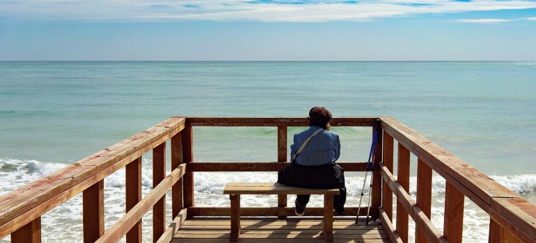 A man sits on a pier and looks out to sea.